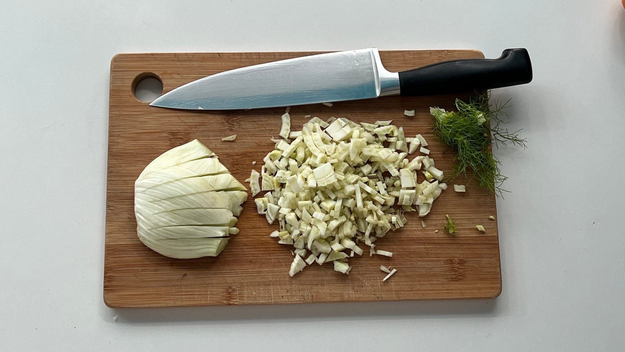 Half a fennel bulb finely chopped on a board, with a chef’s knife and fennel fronds beside it