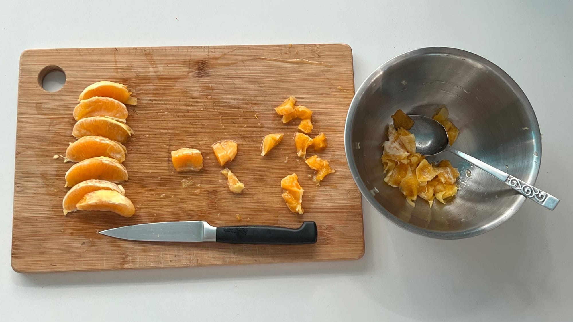 Orange segments and chopped pieces laid out on a board, with peel in a metal bowl and a small knife