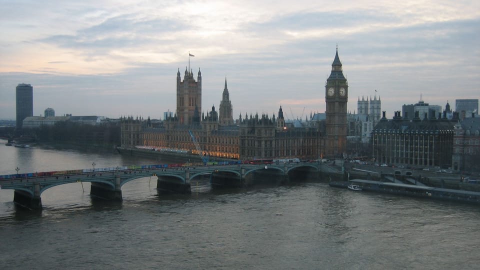 Wide view of the UK Parliament and Big Ben at dusk with Westminster Bridge in the foreground and warm lights reflecting on the Thames.